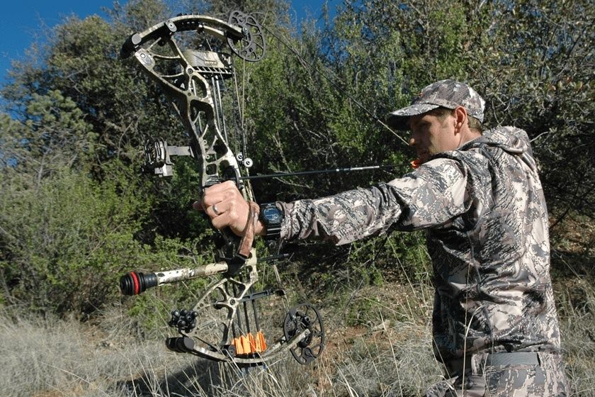 Camouflaged archer draws a compound bow in a wooded clearing
