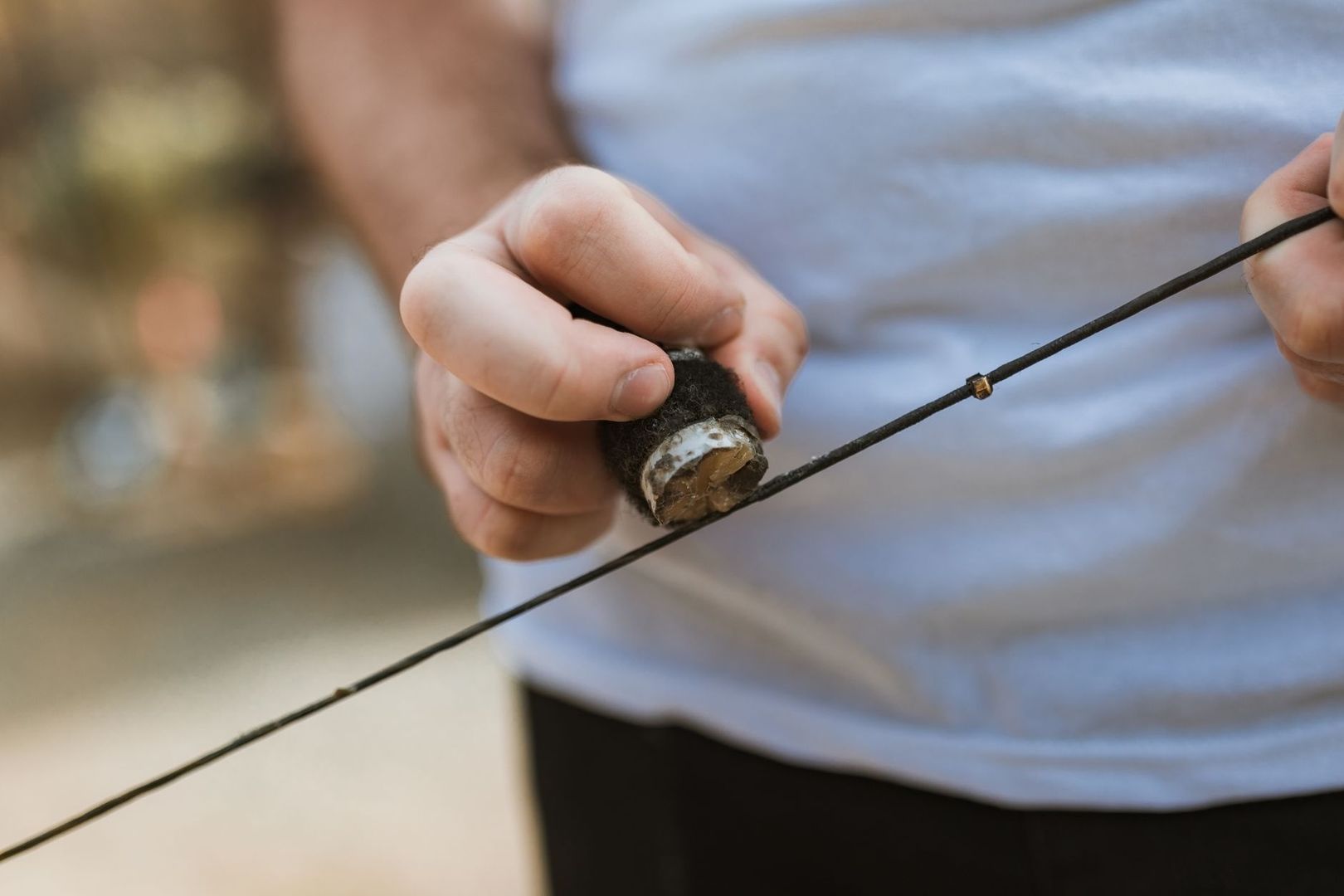 Person applying wax to a dark bowstring with a small wax block